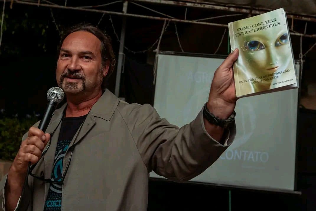 Palestrante ao microfone segurando um livro diante do telão