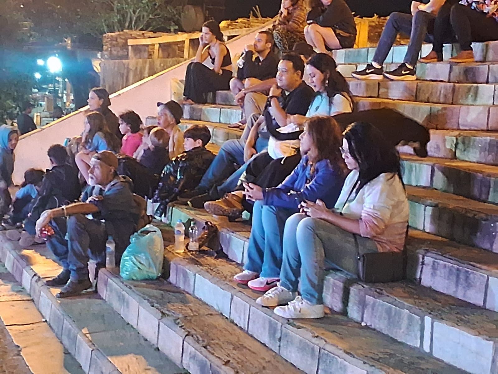 Plateia sentada nos degraus de pedra, à noite, durante um encontro