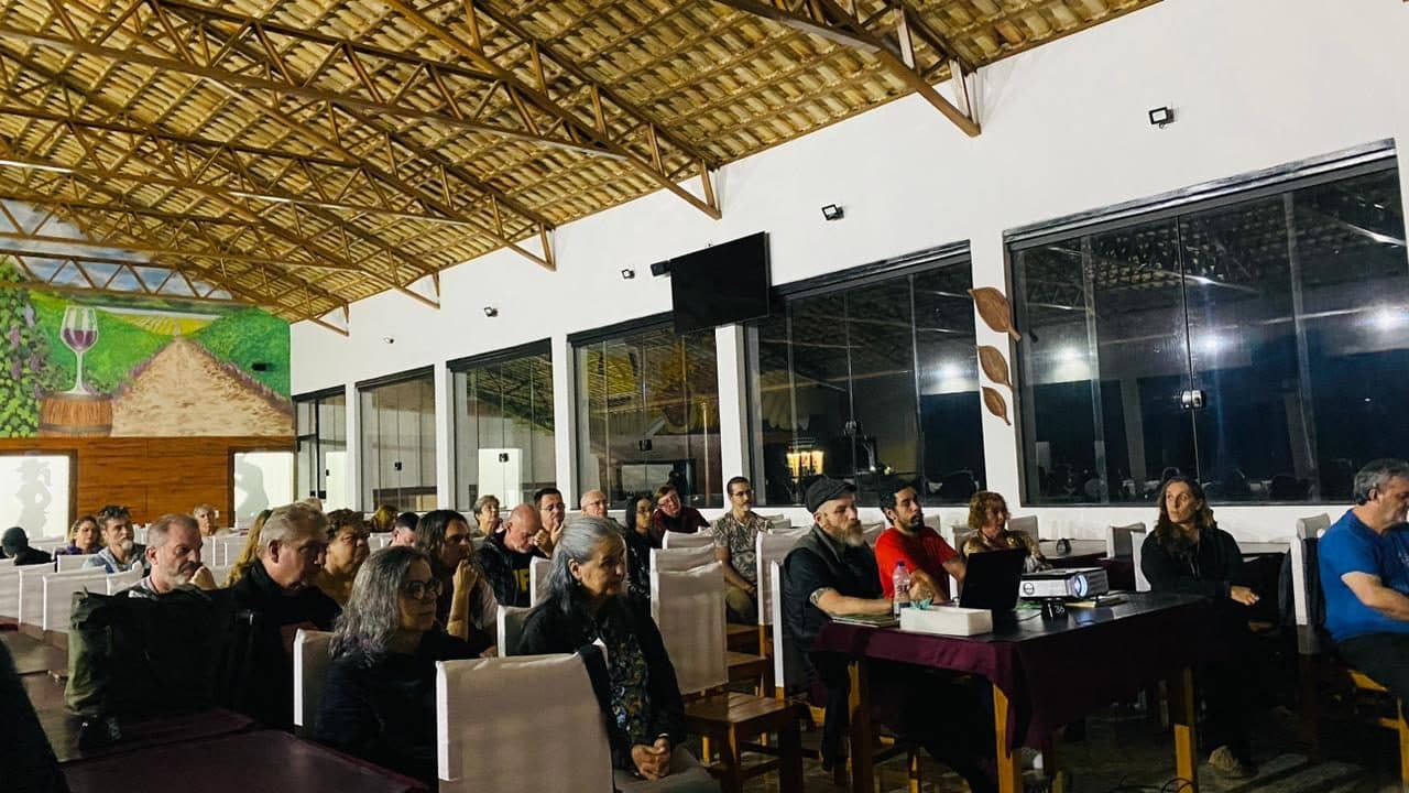 Salão com mesas cheio de participantes durante uma palestra