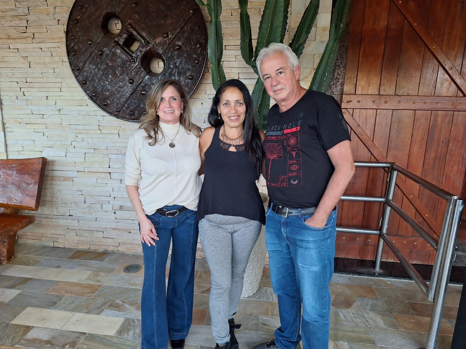 Três participantes posando juntos no saguão de pedra