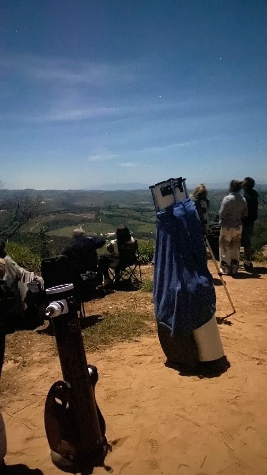 Telescópio montado no alto da serra ao entardecer, com participantes olhando o vale