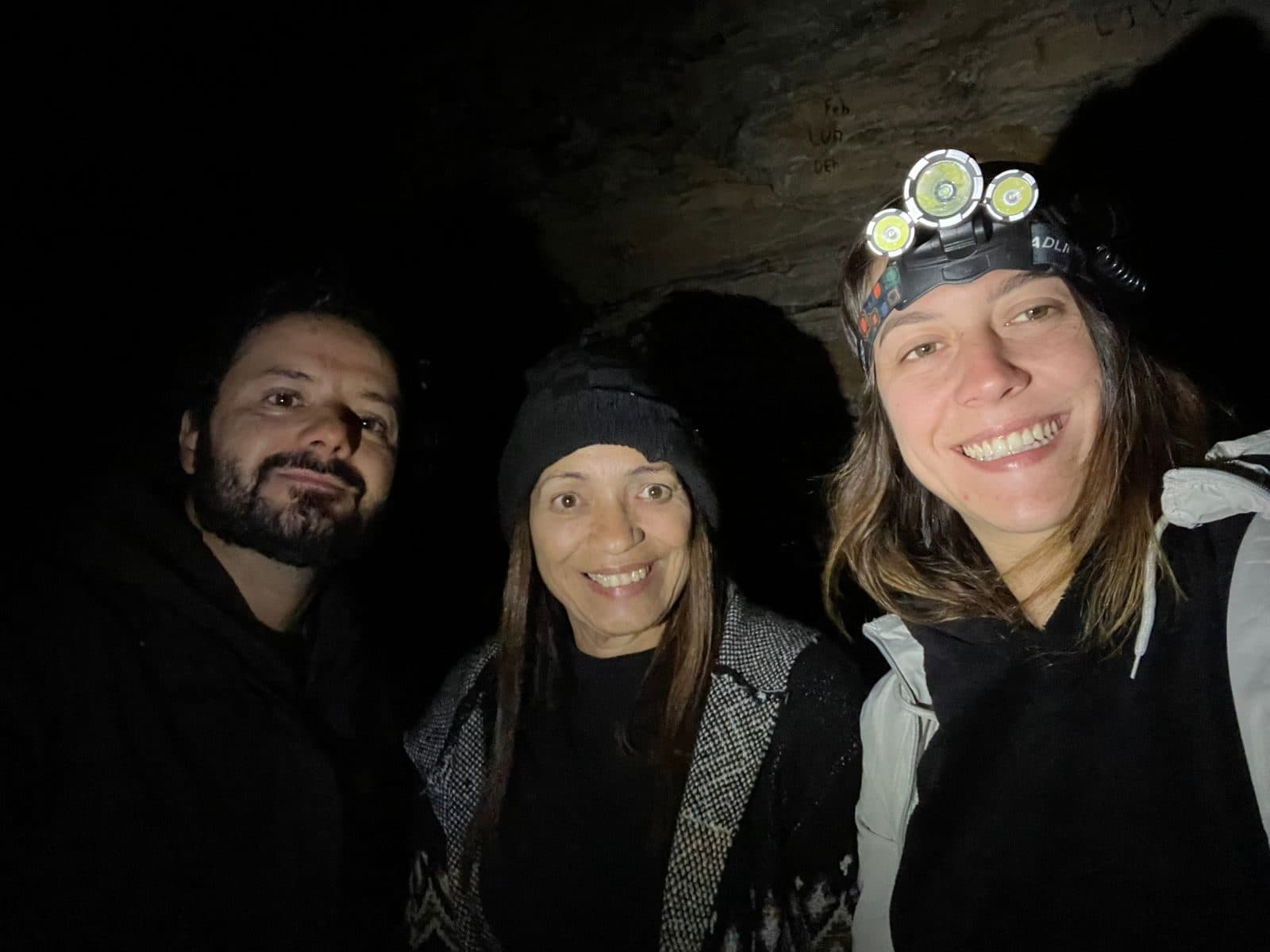 Três participantes sorrindo na pedra, um deles com lanterna de cabeça
