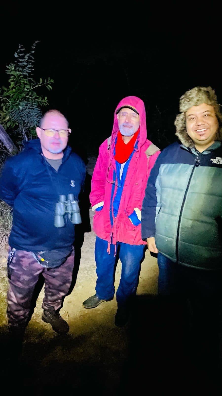 Três participantes agasalhados, com binóculos, de noite