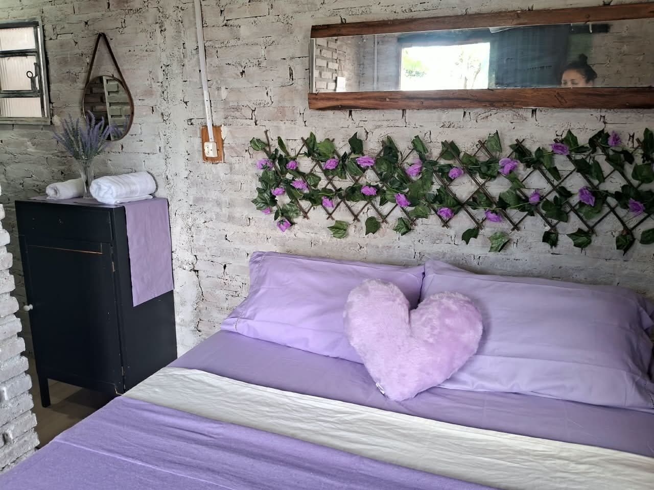 O quarto inteiro, com a cabeceira de flores lilás, o criado-mudo e o espelho