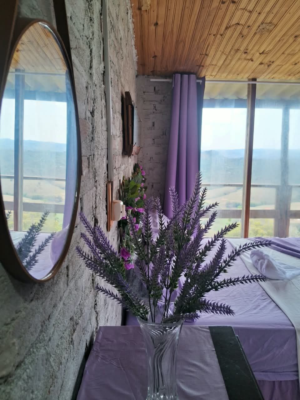 Espelho redondo e vaso de lavanda junto à janela, com o vale ao fundo