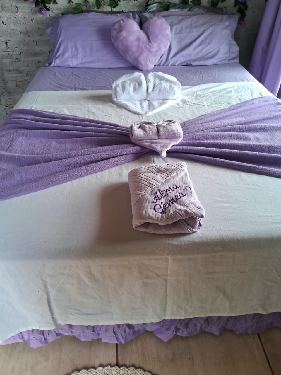 Cama arrumada com toalhas em forma de coração e uma toalha bordada com o nome do chalé