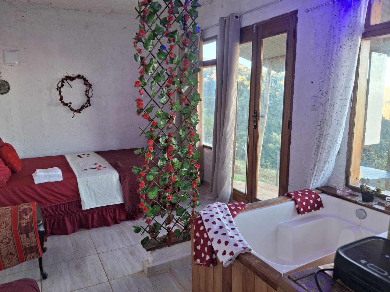Cama com colcha vermelha e coração na parede, perto da porta da varanda